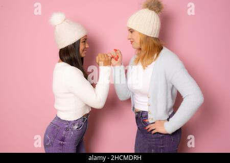 Porträt von zwei jungen Frauen, beste Freunde lächeln einander an, während ein Pinkie Promise Zeichen isoliert auf rosa Hintergrund Stockfoto