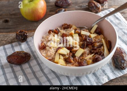 Haferbrei mit Äpfeln und medjool-Datteln in einer Schüssel mit Löffel auf rustikalem und hölzernen Tischhintergrund serviert Stockfoto
