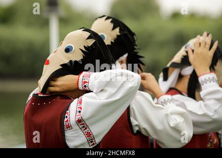 Braila, Rumänien - 26. August 2021: Frauen, die in traditionellen rumänischen Kostümen und mit rituellen Doppelgesichtsmasken gekleidet sind, führen einen traditionellen Tanz auf. Stockfoto