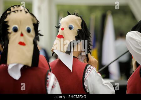 Braila, Rumänien - 26. August 2021: Frauen, die in traditionellen rumänischen Kostümen und mit rituellen Doppelgesichtsmasken gekleidet sind, führen einen traditionellen Tanz auf. Stockfoto