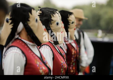 Braila, Rumänien - 26. August 2021: Frauen, die in traditionellen rumänischen Kostümen und mit rituellen Doppelgesichtsmasken gekleidet sind, führen einen traditionellen Tanz auf. Stockfoto