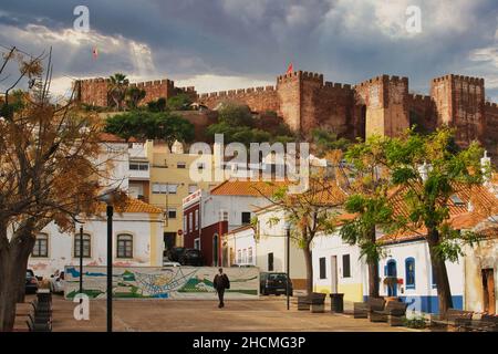 Die alte portugiesische Stadt Silves, dominiert vom riesigen Castelo dos Mouros. Im Vordergrund ein kleiner Platz und traditionelle Häuser Stockfoto