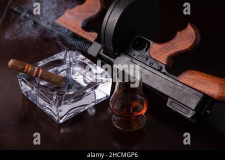 Vintage Thompson Maschinengewehr auf einem dunkelbraunen Tisch mit Zigarre und Whiskey Stockfoto