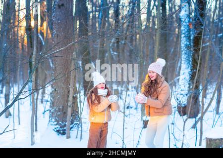 Zwei Mädchen im Teenageralter, die Spaß beim Spielen mit Schnee haben, Schneebälle werfen, eine Schneeschlacht haben. Schnee-Spiele. Winterurlaub. Stockfoto