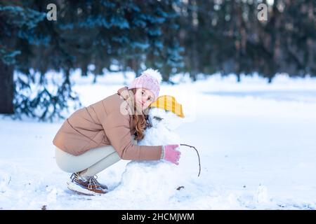 Nettes kleines Teenager-Mädchen mit Spaß spielen machen Schneemann im verschneiten Winterwald. Schnee-Spiele. Winterurlaub. Stockfoto