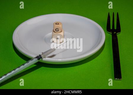 Konzeptbild für die 1G-Kontrolle, weißer Würfel aus dem Jahr 1G mit einer Impfspritze auf einer withe plate vor grünem Hintergrund Stockfoto