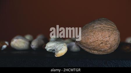 Cashewnüsse, Pistazien, griechischer Nussbaum und Mandeln, abstrakte Tapete, auf rotem Hintergrund Stockfoto