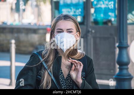 Schöne blonde blaue Augen Mädchen trägt schützende medizinische FFP2 Maske und zu Fuß in der Stadt während Covid oder Coronavirus Stockfoto