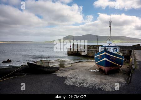 Der Pier am Rinroe Point, in der Nähe von Carrowteige, Irland. Ein Angler steht mit seiner Angelrute am Ende des Piers. Zwei Boote sind an Land. Stockfoto