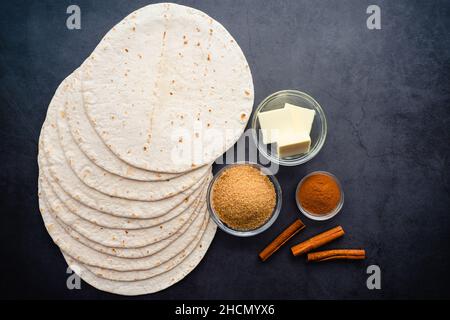 Ansicht von oben Zimtzucker Tortilla Chips Zutaten: Mehl Tortillas, Butter, brauner Zucker und Zimt auf einem dunklen Hintergrund