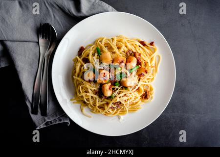 Pasta Carbonara mit Linguine und garniert mit in der Pfanne gebratenen Jakobsmuscheln: Nudeln in einer cremigen Sauce mit Parmigiano Reggiano und Eigelb garniert w Stockfoto
