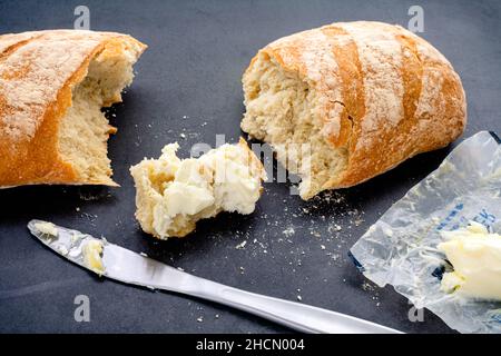 Gebuttertes Stück frisch gebackenes Baguette: Französisches Brot mit Butter auf dunklem Grund Stockfoto