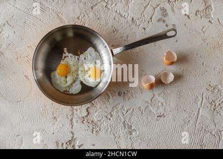 Gebratene zwei Eier in Kupferpfanne auf rauem texturiertem Lehm-Hintergrund. Gesundes Frühstückskonzept. Stockfoto