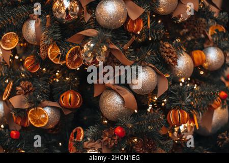 Getrocknete Mandarinen, Orangen, Tannenzapfen Weihnachtskugeln hängen an den Christbaumzweigen. Gemütliche Winterdetails und goldene Bokeh-Lichter. Winter Stockfoto