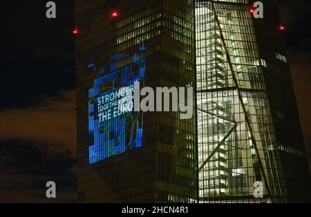 30. Dezember 2021, Hessen, Frankfurt/Main: Bei einem Testlauf wird die Aufschrift „Sronger together with the Euro“ auf die Südfassade des Hauptquartiers der Europäischen Zentralbank (EZB) im Frankfurter Ostende projiziert. Vor 20 Jahren wurde am Silvesterabend in zwölf EU-Ländern die einheitliche europäische Währung, der Euro, eingeführt. Für Deutschland bedeutete dies, Auf Wiedersehen zur D-Mark zu sagen. Vom 31. Dezember 2021 bis zum 9. Januar 2022 wird die Fassade der EZB in den Abendstunden beleuchtet. Foto: Arne Dedert/dpa Stockfoto