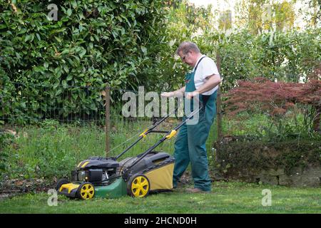 Mann schiebt Rasenmäher durch kleinen Hinterhof im Frühjahr, etwas vom Rasen zu entfernen. Stockfoto