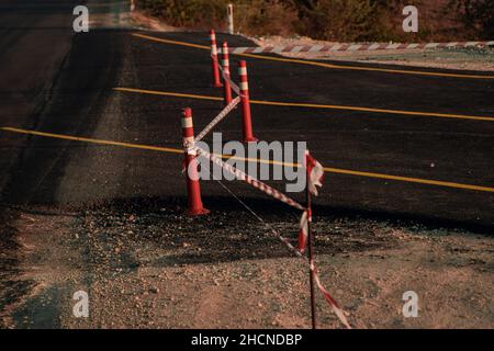 Vorübergehende Straßensperren, Straßenreparatur, Straßenbau. Die neue Straße wird vom Band blockiert, über die Stangen, die Fahrspur, den Asphalt gespannt Stockfoto