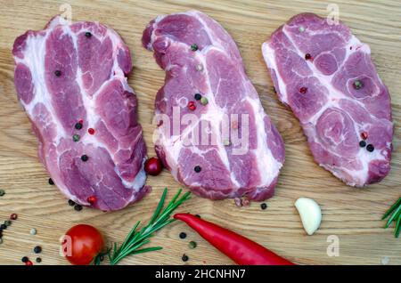 Drei saftige Steaks liegen neben roten und grünen Chilischoten und frischem grünen Salat auf einem Holztisch. Stockfoto