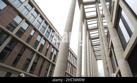 Fassade eines Gebäudes mit Marmorsäulen. Blick von unten auf einen modernen architektonischen Komplex, ein neues Gebäude mit hellbeigen Säulen und großen Fenstern. Stockfoto