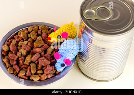 Braune knusprige Bio-Kitty-Kibble-Stücke in einer Schüssel, Spielzeugmäuse und nasses Katzenfutter aus Metalldose für Tierfutter auf hellem Hintergrund. Stockfoto
