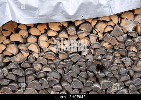 Gestapelter Holzstapel für Brennholz unter grauer Plane. Stockfoto