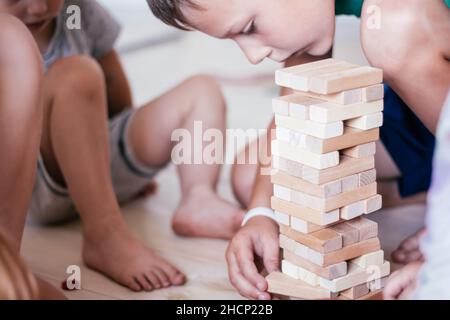 Verschwommene Kinderhände spielen Spiel mit Turm aus Holzblöcken Stockfoto