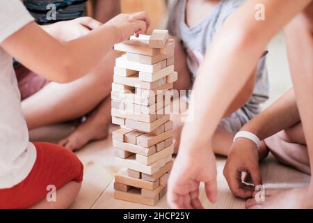 Verschwommene Kinderhände spielen Spiel mit Turm aus Holzblöcken Stockfoto