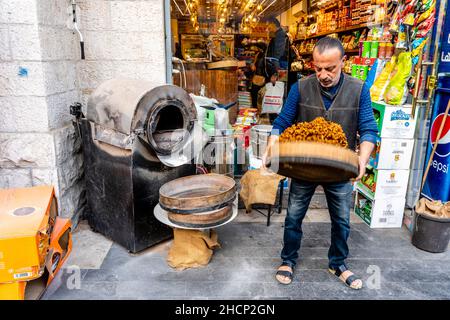 Ein Mann, der Nüsse/Samen vor einem Geschäft in der Innenstadt von Amman, Amman, Jordanien, röstet. Stockfoto