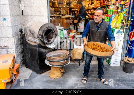 Ein Mann, der Nüsse/Samen vor einem Geschäft in der Innenstadt von Amman, Amman, Jordanien, röstet. Stockfoto