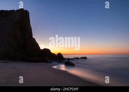 Strand in Malibu, Kalifornien im Morgengrauen. Klippen von Point Dume im Hintergrund; ruhiger Strand und glattes Meer im Vordergrund. Stockfoto