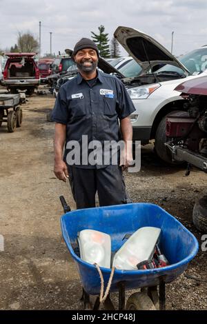 Ein Mann posiert mit den Teilen, die er aus einem Junk-Auto auf dem LKQ Pick Your Part Auto Bergungshof in Fort Wayne, Indiana, USA entfernt. Stockfoto