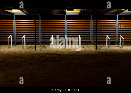 Ein leerer Fahrradstand wurde während einer Pandemie im Stadtpark vergossen. Treffpunkte ohne Menschen. Das Foto wurde in der Nacht mit künstlicher Straßenbeleuchtung aufgenommen Stockfoto