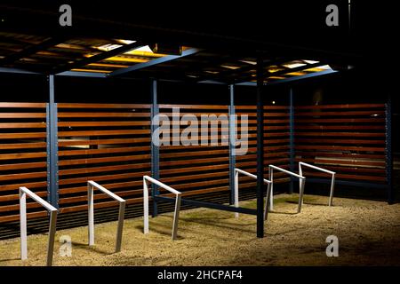 Ein leerer Fahrradstand wurde während einer Pandemie im Stadtpark vergossen. Treffpunkte ohne Menschen. Das Foto wurde in der Nacht mit künstlicher Straßenbeleuchtung aufgenommen Stockfoto