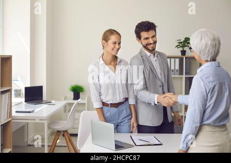 Glückliches Ehepaar, das sich mit einer Rechtsanwältin, immobilienmaklerin oder Finanzberaterin die Hände schüttelte. Stockfoto