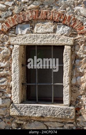 Detail eines alten Fensters mit einem eisernen Metallgitter an einer alten Wand aus Kieselsteinen. Apuanische Alpen, Toskana, Italien, Europa. Stockfoto