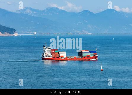 Rotes Containerschiff im Golf von La Spezia beim Verlassen des Hafens, im Hintergrund die Küste und die Apuanischen Alpen. Ligurien, Italien, Europa Stockfoto