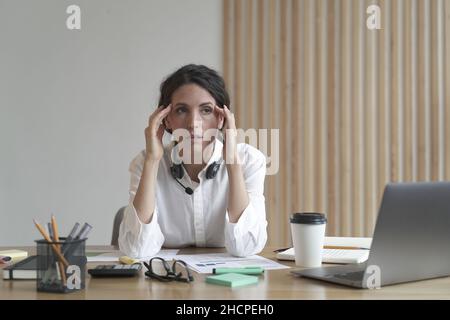 Frustrierte Geschäftsfrau, die sich müde fühlt, während sie im Büro sitzt und Kopfschmerzen bei der Arbeit hat Stockfoto