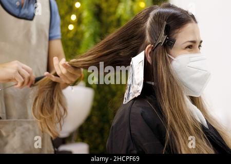 Professioneller Friseur, der einem Mädchen auf dem Rücken in einem Friseurstuhl Höhepunkte zeigt Stockfoto