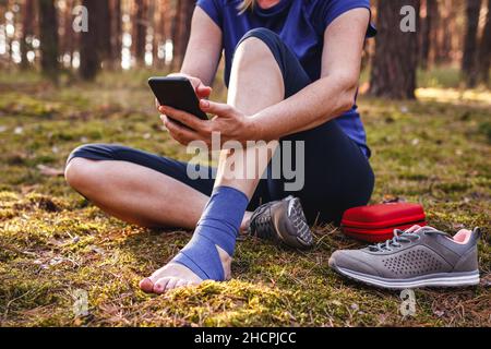 Verletzte Wanderer mit Verstauchung Knöchel mit Smartphone Hilfe zu bekommen. Frau gab sich erste Hilfe bei Wanderverletzungen in der Natur Stockfoto