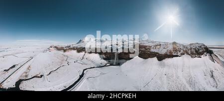 Luftdrohnenaufnahme des Seljalandsfoss Wasserfalls in Island, aufgenommen im Winter. Blick von oben auf den majestätischen nordischen Wasserfall mit Touristen von oben. Winter Stockfoto