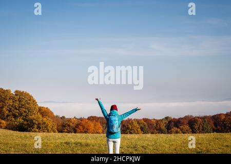 Wandern im Freien in der Herbstsaison. Genuss der Herbstwanderung in der Natur. Glückliche Frau Tourist mit Rucksack und Arme ausgestreckt Blick auf schöne Szene Stockfoto