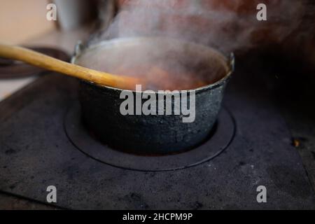 Gusseiserner Kessel kocht einen Gulasch-Eintopf über einem Holzofen aus roten Ziegeln im Hinterhof eines ländlichen Hauses in Rumänien. Stockfoto