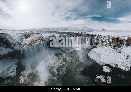 Drohnenaufnahme des Godafoss Wasserfalls, Island, aus einem hohen Winkel aufgenommen. Luftaufnahme der mächtigen Kaskade, des Flusses und der schneebedeckten Felsen. Spätherbst Stockfoto