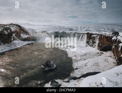 Drohnenaufnahme des Godafoss Wasserfalls, Island, aus einem hohen Winkel aufgenommen. Luftaufnahme der mächtigen Kaskade, des Flusses und der schneebedeckten Felsen. Spätherbst Stockfoto