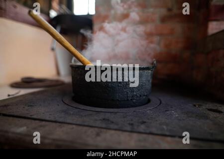 Gusseiserner Kessel kocht einen Gulasch-Eintopf über einem Holzofen aus roten Ziegeln im Hinterhof eines ländlichen Hauses in Rumänien. Stockfoto