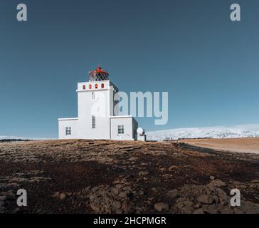 Panoramabild des Leuchtturms von Cape Dyrholaey mit Schnee und Morgenlicht mit blauem Himmel. Winter in Island. Stockfoto