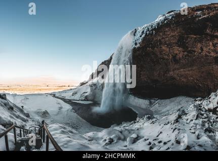 Seljalandsfoss Wasserfall in Island im Winter mit blauem Himmel und Schnee und gefrorener Landschaft. Stockfoto