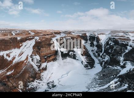 Luftdrohnenaufnahme des Haifoss Wasserfalls in Island im Winter in den Highlands. Blauer Himmel und Wolken im Schnee.