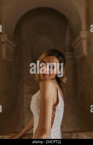 Vertikal einer fröhlichen, schönen Braut aus dem Nahen Osten, die in ihrem weißen Hochzeitskleid posiert Stockfoto