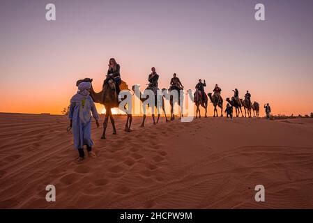 Beduinen führen Kamelkarawane mit Touristen durch den Sand in der Wüste Stockfoto